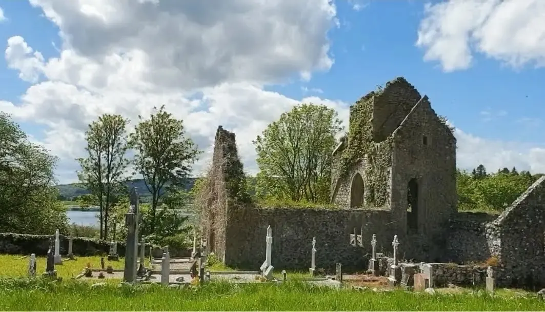 Stone ruins and grave markers beside trees under a bright sky.